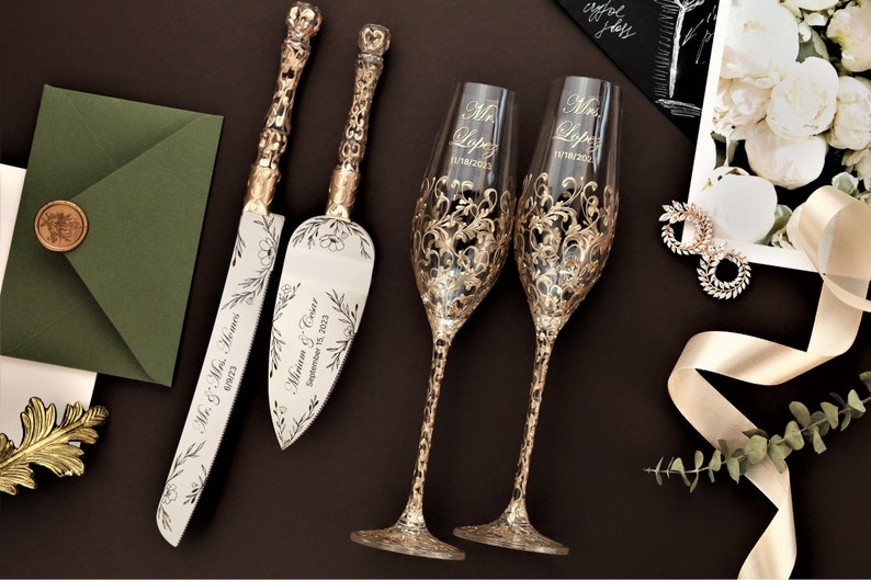 May include: A wedding cake cutting set featuring a knife and server, both with gold handles and floral designs. The set is personalised with the names "Mr. & Mrs. Lopez" and the date "September 10, 2023". Two champagne flutes with gold floral designs and the same names and date are also included.