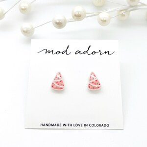 May include: A pair of Christmas tree stud earrings on a white card. The earrings are pink with white and red accents, and green dots. The card reads "mod adorn" and "HANDMADE WITH LOVE IN COLORADO."