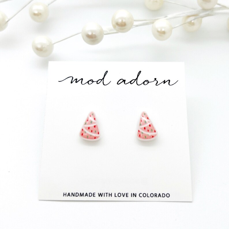 May include: A pair of Christmas tree stud earrings on a white card. The earrings are pink with white and red accents, and green dots. The card reads "mod adorn" and "HANDMADE WITH LOVE IN COLORADO."
