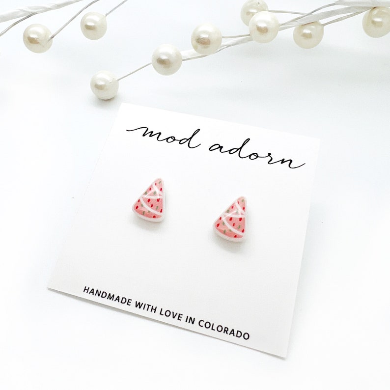 May include: A pair of watermelon slice earrings on a white card. The earrings are pink with white and red details. The card reads "mod adorn" and "HANDMADE WITH LOVE IN COLORADO".