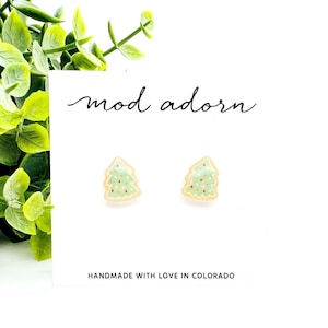 May include: A pair of small, green and white Christmas tree earrings on a white card with the text "mod adorn" and "handmade with love in Colorado".