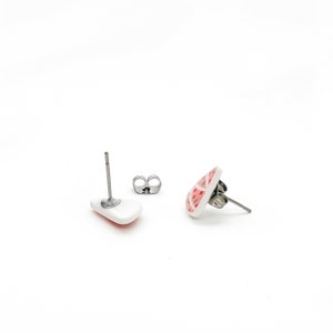May include: White ceramic stud earrings with a red and pink geometric pattern. The earrings have stainless steel posts and butterfly backs. The earrings are displayed on a white background.