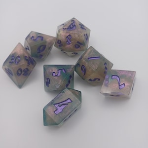 May include: Set of seven iridescent dice with purple numbers. The dice are a light green and brown color with a pearlescent finish.