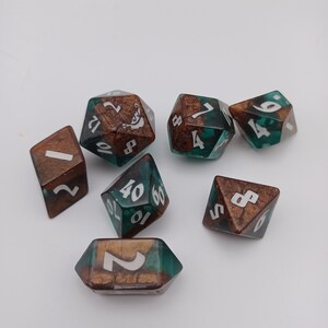 May include: Set of seven green and brown dice with white numbers. The dice are made of resin and have a speckled appearance.