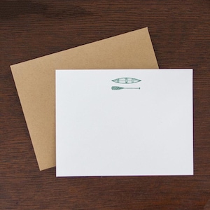 May include: A white card with a green illustration of a canoe and paddle. The card is on top of a brown envelope.