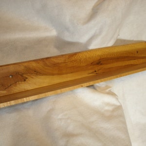 Op de afbeelding: Een houten plank met een natuurlijke houten afwerking. De plank is schuin en heeft een uniek houtnerfpatroon.