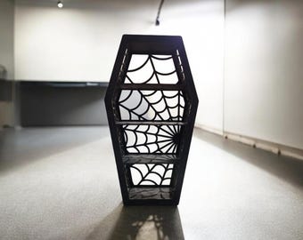 May include: Black coffin-shaped shelf with a spiderweb design. The shelf has four shelves and is made of wood.
