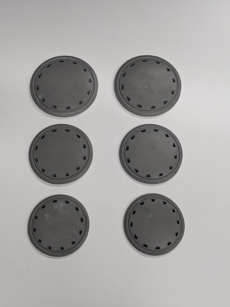 Puede incluir: Seis posavasos redondos de pl&aacute;stico gris con un patr&oacute;n decorativo alrededor del borde.