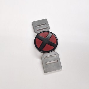 以下が含まれることがあります： 赤と黒のX字型のロゴが付いた銀色のベルトバックル