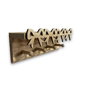 May include: Wooden wall-mounted coat rack with a natural finish. The rack features a row of decorative bow cutouts along the top edge and four wooden pegs for hanging items. The design is simple and rustic.