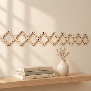 May include: A horizontal wooden wall decoration featuring a repeating quatrefoil pattern. The piece consists of eight connected, light-colored wooden shapes with smooth edges, mounted flat against a plain, neutral-toned wall surface.