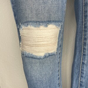 May include: Light blue denim jeans with a distressed knee featuring a white mesh patch.