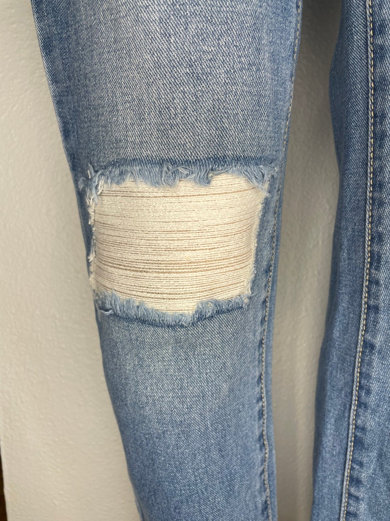 May include: Light blue denim jeans with a distressed knee featuring a white mesh patch.