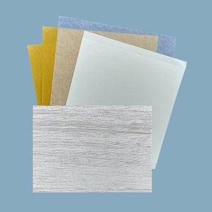 May include: A stack of different colored paper sheets, including blue, brown, and gold, on top of a white textured surface.