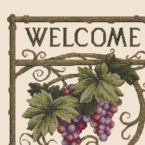 以下が含まれることがあります： WELCOME FRIENDSと書いてある茶色の文字の入った木製の看板。看板は緑の葉と紫のブドウのついたブドウのつるで飾られています。