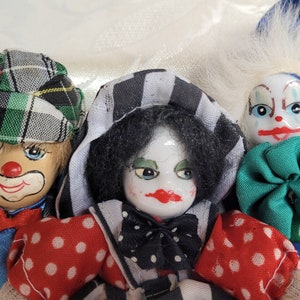 Puede incluir: Tres muñecas payaso de porcelana con caras pintadas y ropa colorida. Las muñecas llevan sombreros y tienen diferentes colores de pelo. Una muñeca lleva un sombrero de cuadros verde y blanco, otra lleva un sombrero de rayas negras y blancas y la tercera lleva un sombrero azul y blanco.