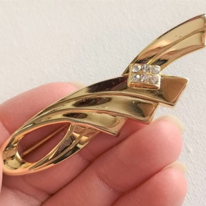 May include: A gold-toned brooch with a geometric design and a clear rhinestone accent.