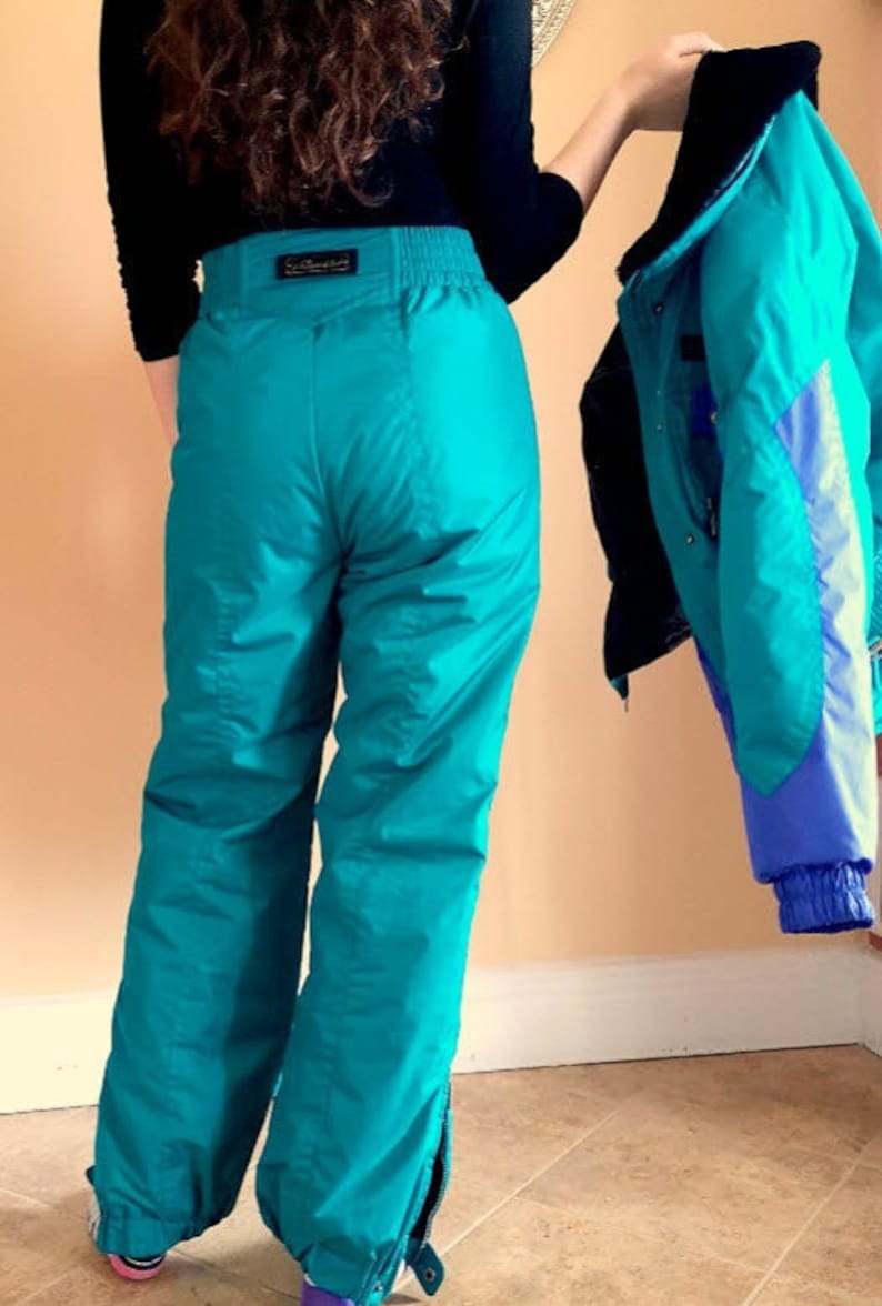 Puede incluir: Pantal&oacute;n de esqu&iacute; de color turquesa con cintura negra y cremallera lateral. El pantal&oacute;n est&aacute; hecho de un material brillante y resistente al agua.