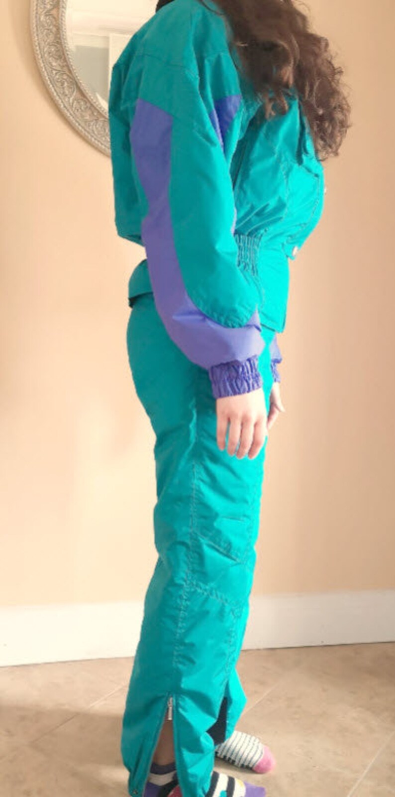 Puede incluir: Un traje de esqu&iacute; turquesa y morado con una cremallera en el lateral de la pierna.