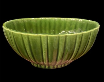 May include: A green ceramic bowl with a ribbed exterior. The bowl has a glossy finish and a rounded shape. The color is a vibrant, medium green. The bowl is likely for serving food or as a decorative piece.