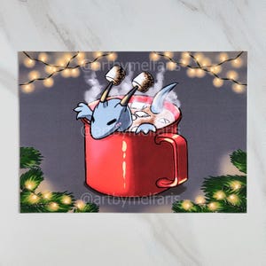 May include: An illustration of a blue dragon in a red mug of hot chocolate, topped with marshmallows. The image has a festive feel, with fairy lights and greenery in the background. The dragon is the central focus.