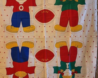 May include: A white fabric panel featuring a repeating pattern of printed doll shapes and footballs. The dolls wear red or green shirts with blue or red pants and yellow shoes. Small red stars are scattered across the white background.