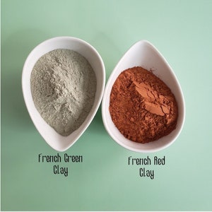May include: Two white bowls filled with powder. The bowl on the left contains green powder labeled "French Green Clay". The bowl on the right contains red powder labeled "French Red Clay".