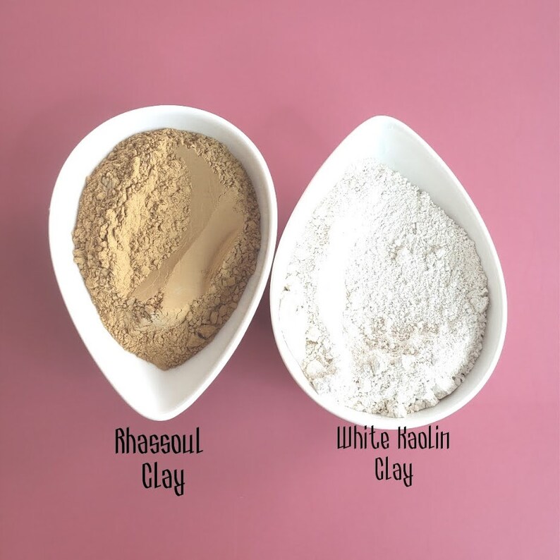 May include: Two white bowls filled with different types of clay. The bowl on the left contains a light brown clay labeled "Rhassoul Clay". The bowl on the right contains a white clay labeled "White Kaolin Clay".