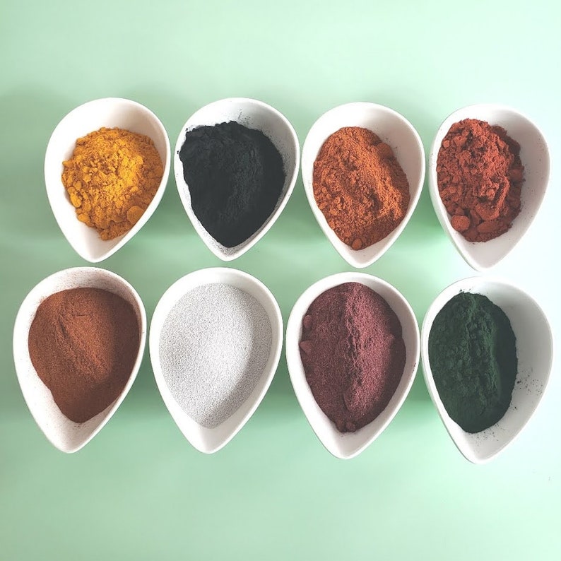 May include: Eight small white bowls, each containing a different colored powder. The powders are: yellow, black, orange, red, brown, gray, purple, and green.