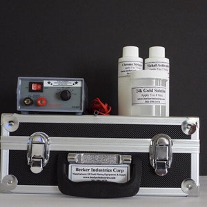 May include: A silver metal carrying case with a black interior and a handle. The case contains a small electronic device with a red switch, two bottles of liquid, and a jar of gold solution. The bottles are labeled "Chrome Stripper" and "Nickel Activation". The jar is labeled "24k Gold Solution". The text on the case reads "Becker Industries Corp. Manufacturer of Gold Plating Equipment & Supply www.beckerindustries.com 561-994-1070".