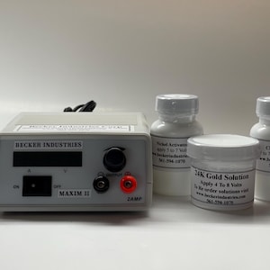 Peut inclure: Un bloc d'alimentation blanc avec un écran numérique, étiqueté "Becker Industries Maxim II 2 Amp". Trois flacons blancs avec des étiquettes sont devant l'appareil. Les étiquettes indiquent "Nickel Activator", "24K Gold Solution" et "Chrome Stripper".