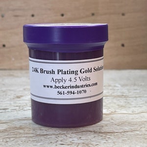 May include: A purple jar with a white label that reads "24K Brush Plating Gold Solution Apply 4.5 Volts www.beckerindustries.com 561-594-1070."