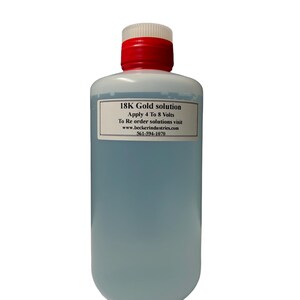 Puede incluir: Una botella de plástico transparente con una tapa roja y blanca, llena de un líquido azul claro. Una etiqueta blanca muestra el texto "18K Gold solution" e instrucciones. La botella está sobre un fondo blanco.