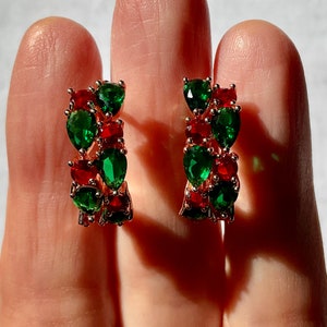 Peut inclure: Une paire de boucles d'oreilles créoles en or avec des pierres précieuses en forme de poire rouges et vertes alternées.