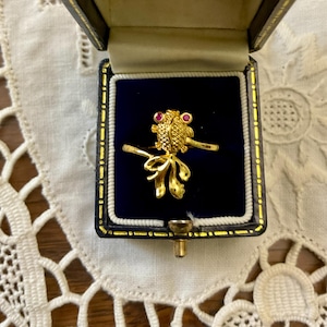 Peut inclure: Une bague en or avec un motif de hibou détaillé et deux pierres précieuses rouges pour les yeux. La bague est dans un écrin en velours bleu.