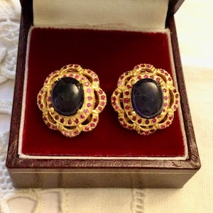 Peut inclure: Une paire de boucles d'oreilles en or avec une pierre ovale bleu foncé entourée de petites pierres roses dans un motif floral.
