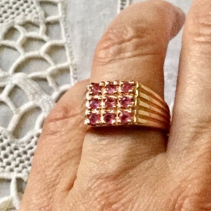 Peut inclure: Une bague en or avec un sertissage carré orné de neuf pierres précieuses roses. La bague a une bande texturée.