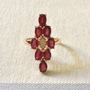 Peut inclure: Une bague en or avec un groupe de pierres précieuses ovales rouges et un diamant rond unique au centre.