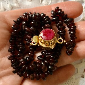 Peut inclure: Un collier en or avec un pendentif en pierre rouge. Le collier est composé de petites perles rouge foncé et possède un fermoir en or.