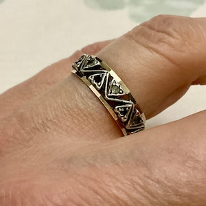 May include: A silver ring with a geometric design featuring black and white stones. The ring is worn on a finger.