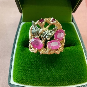 Peut inclure: Une bague en or ornée de pierres précieuses rubis de forme ovale. La bague présente un motif floral avec des feuilles et de petits accents de rubis. La bague est présentée dans un écrin en velours vert.