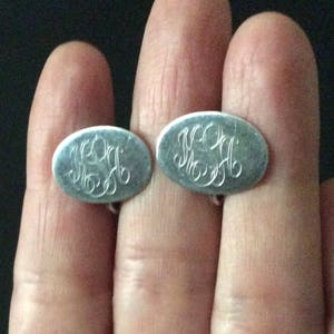 Peut inclure: Une paire de boutons de manchette en argent avec des initiales gravées. Les boutons de manchette sont de forme ovale et ont une finition lisse et polie.