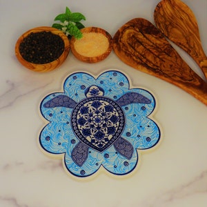 May include: A blue and white ceramic trivet shaped like a flower with a blue and white sea turtle design in the center.
