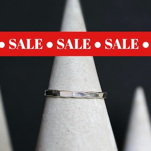 May include: A silver hammered band ring on a gray concrete display stand. The ring is simple and modern in style.