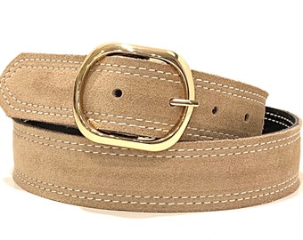 May include: A beige suede belt with a gold oval buckle and white stitching. The belt is rolled up and the buckle is in focus.