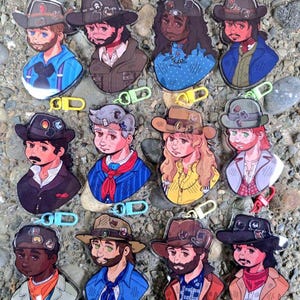 May include: A collection of twelve acrylic keychains featuring illustrated characters wearing cowboy hats, each attached to a colorful plastic lobster clasp. The characters display various facial features, hair colors, and western-style clothing.