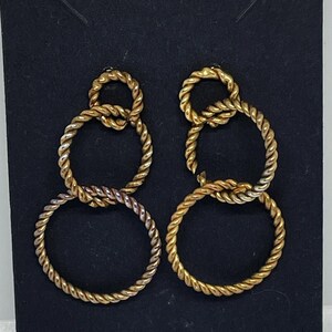 May include: A pair of gold-toned earrings with a twisted rope design. Each earring features three interconnected circles.