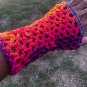 May include: A crocheted arm warmer with a gradient of orange, pink, and purple.