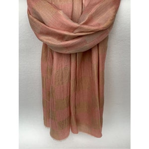 Op de afbeelding: Een zachte, geweven sjaal in roze en bruine tinten. De sjaal is gedrapeerd, wat de textuur en het patroon benadrukt. De stof lijkt lichtgewicht, met een subtiele glans. De randen zijn afgewerkt met een delicate franje.