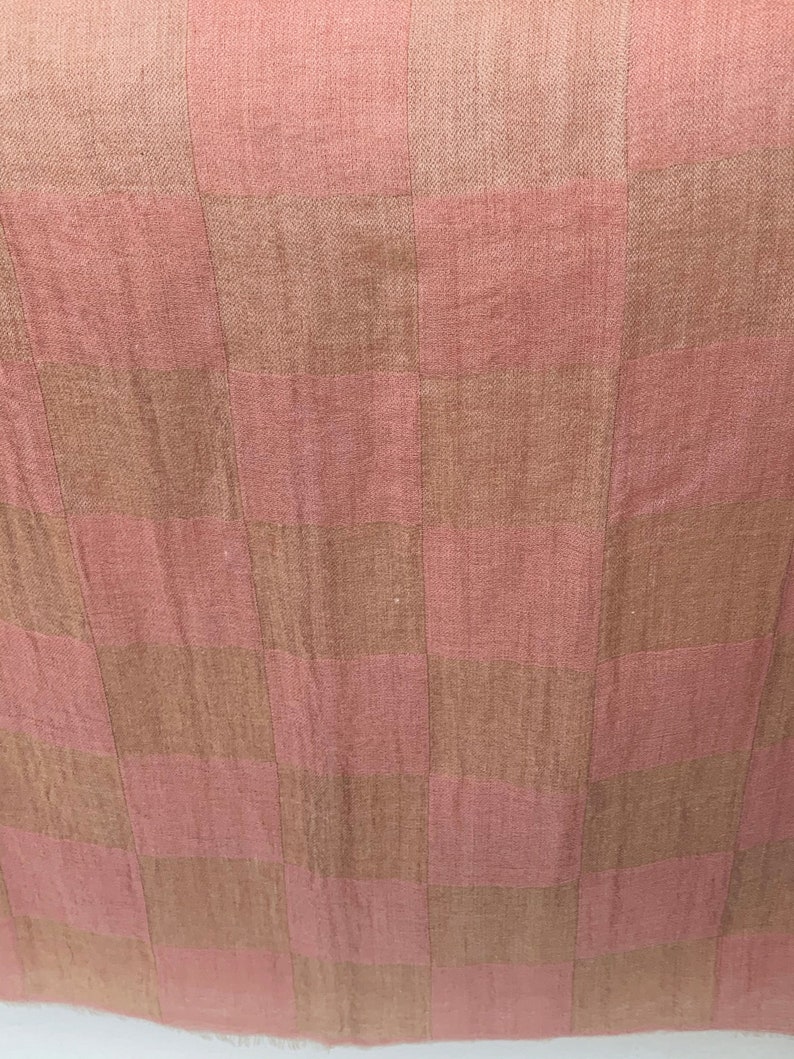 Op de afbeelding: Close-up van een textiel met een geruit patroon. Het patroon wisselt af tussen stoffige roze en bruine vierkanten. De stof heeft een licht getextureerd uiterlijk, wat wijst op een geweven materiaal. De algehele esthetiek is zacht en neutraal.